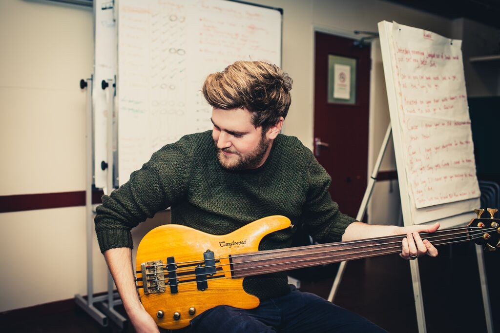 Young man with short blonde hair teaching a guitar workshop