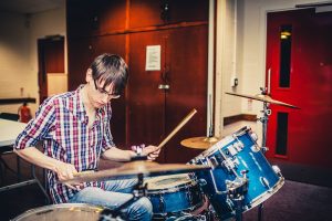 Young man in checked shirt playing the drums at Band Room