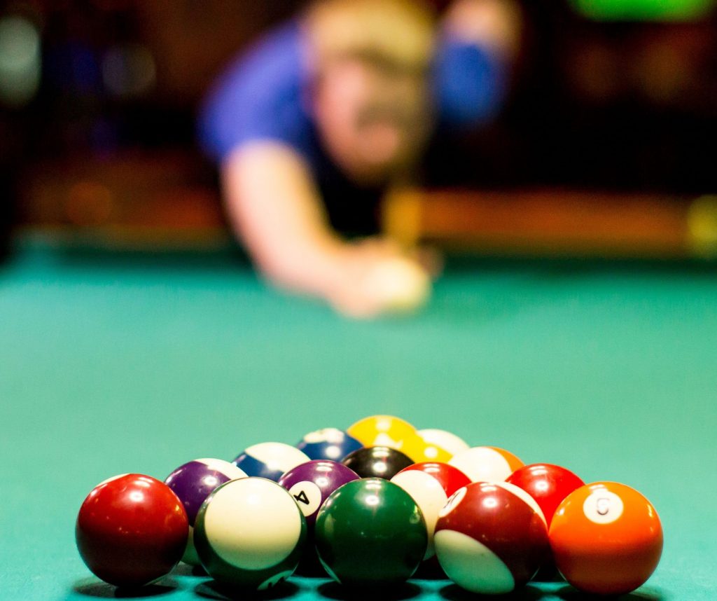Young person with blonde hair and wearing a blue t shirt playing pool