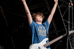 A person with curly hair raises both arms in celebration, partially holding a guitar.