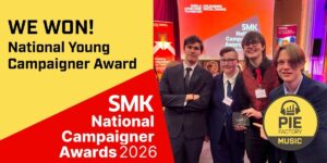 Four young people in formal attire smile and pose together on stage with an award. A large sign reads “WE WON! National Young Campaigner Award” and “SMK National Campaigner Awards 2026.” The Pie Factory Music logo is visible.